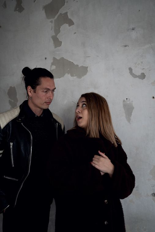 The duo in winter coats, standing close at the wall.